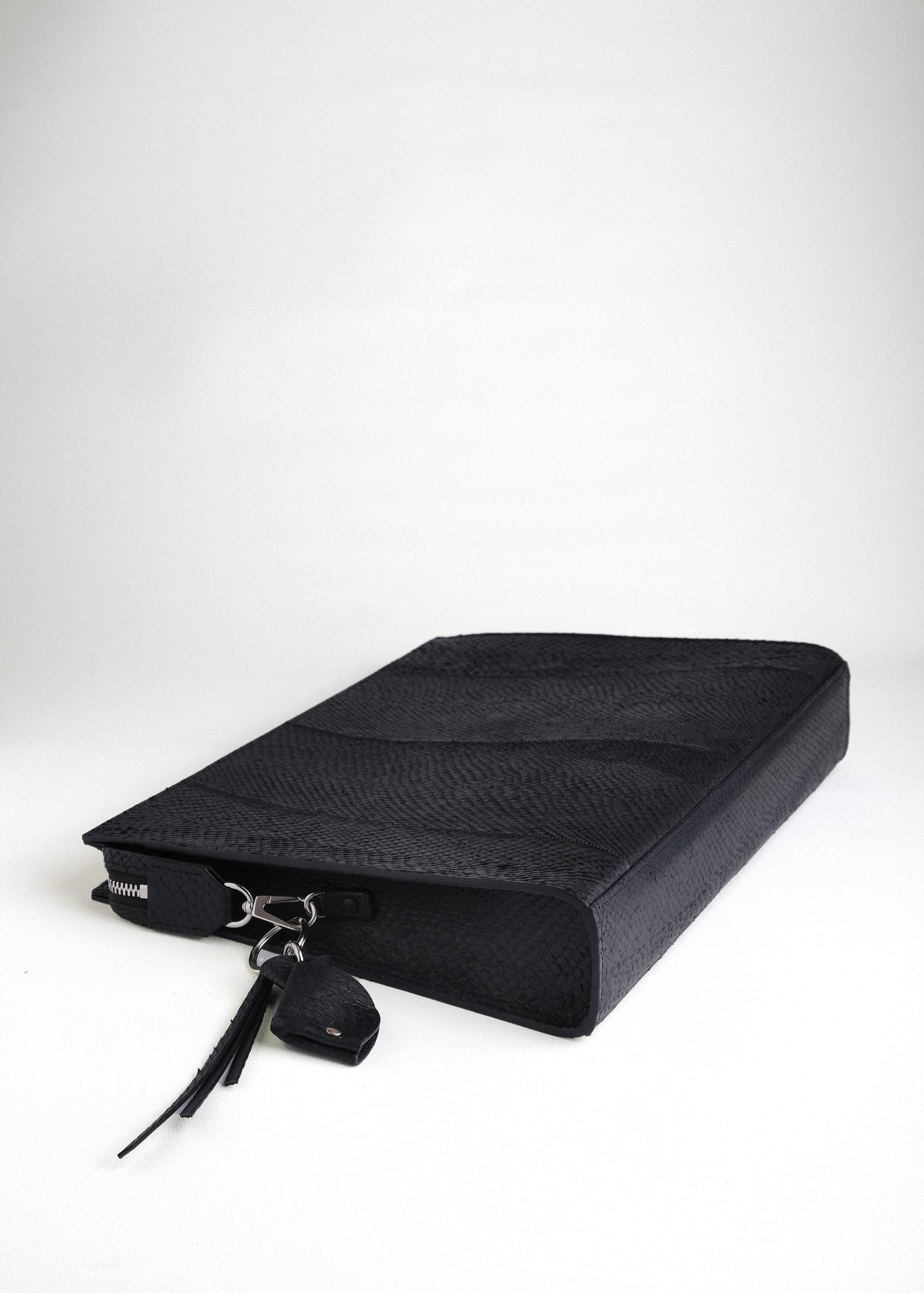 Baltic Clutch lying flat with bottom side visible, featuring detachable fish leather key charm and refined detailing