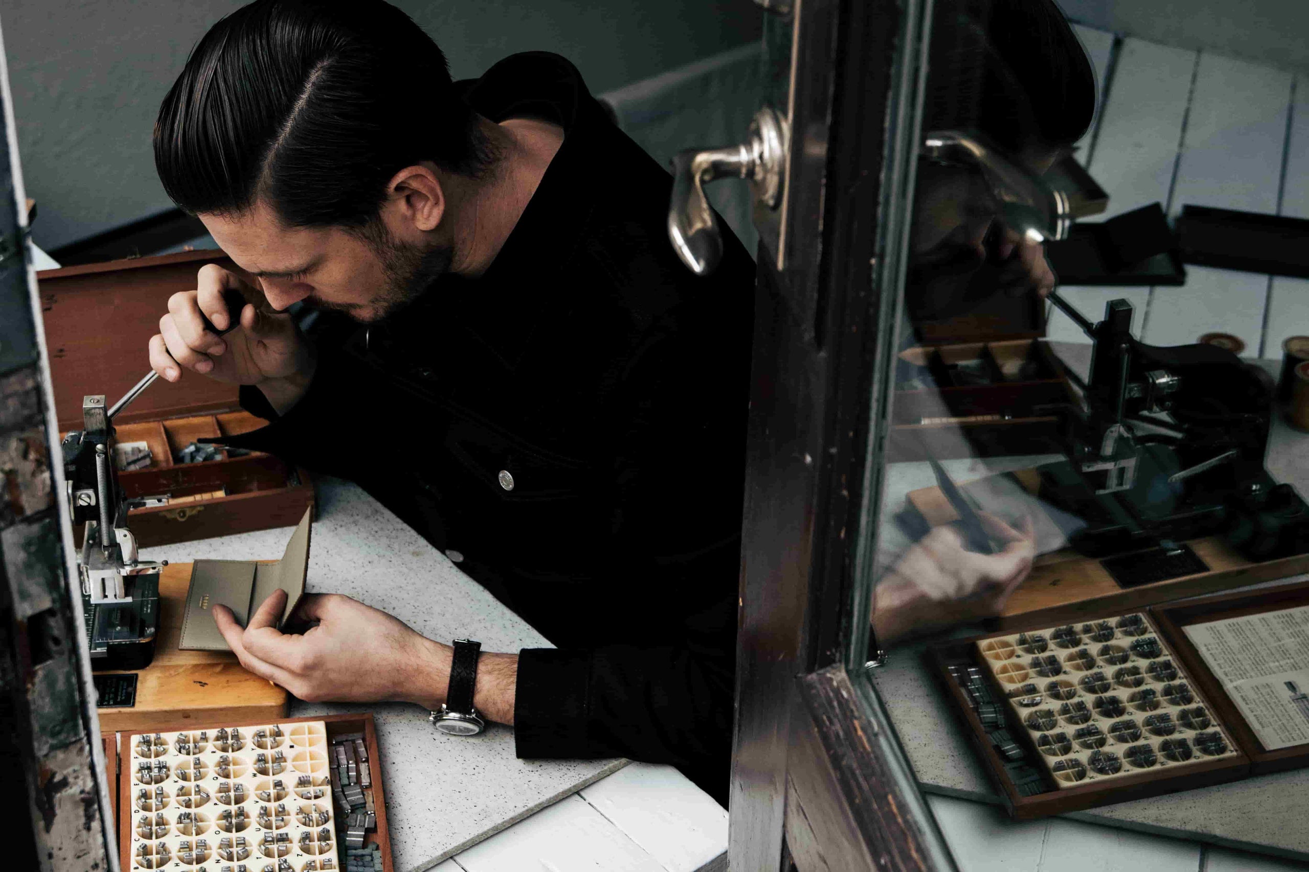 Skilled artisan at Kristian Eddé performing hot stamping embossing on a luxury leather product, adding personalized initials with precision, vertical