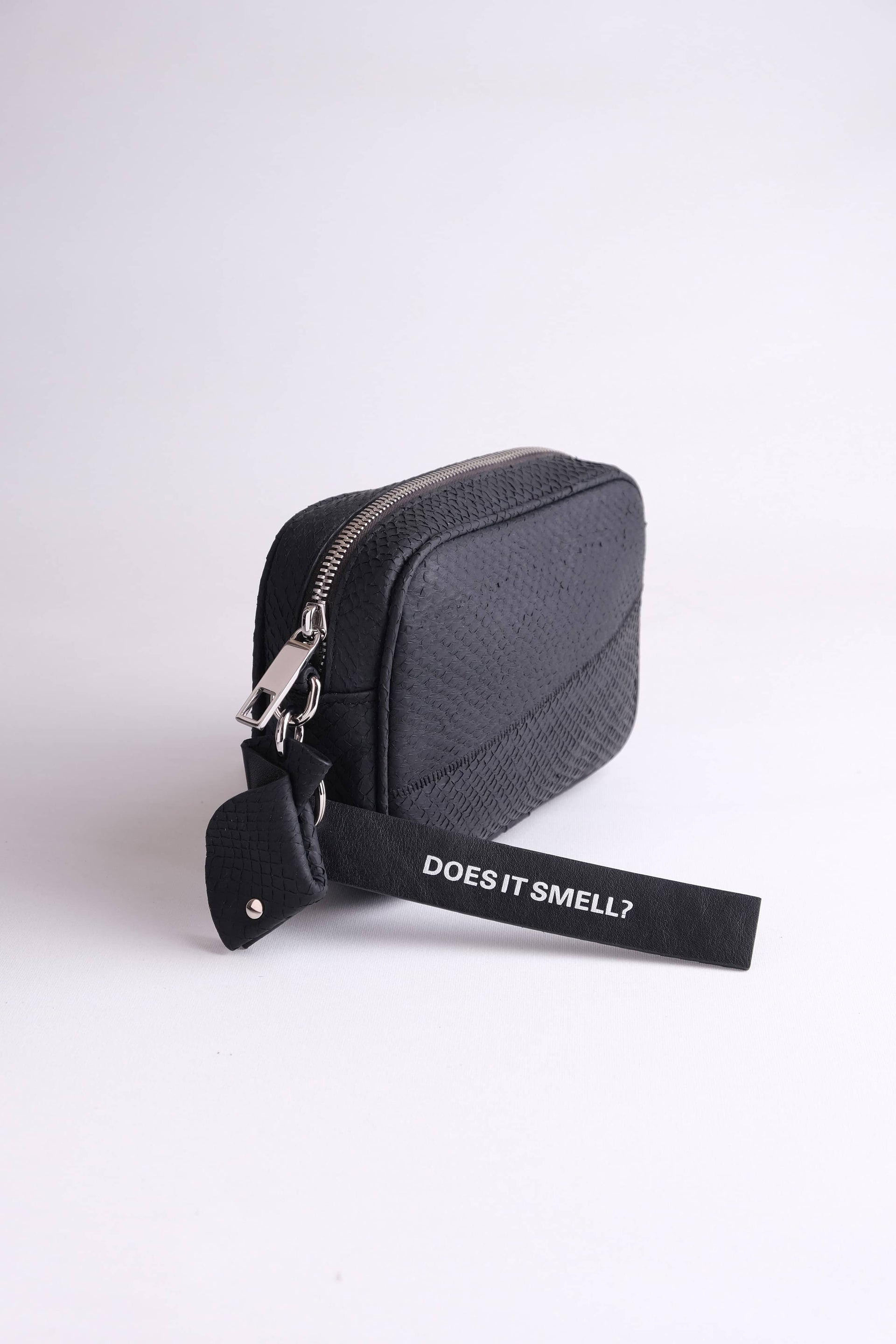 Black fish leather pouch accessory for Kolga camera bag with strap labeled 'Does It Smell?' sustainable design by Kristian Eddé
