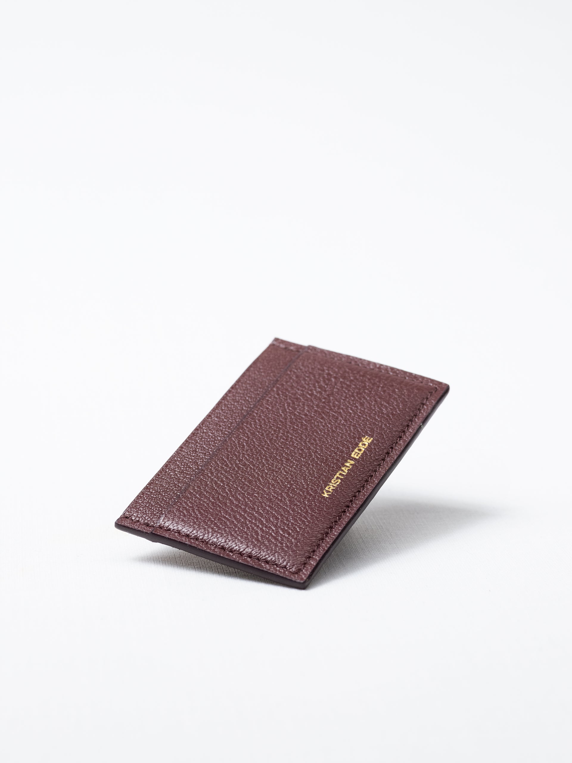 Bothnia burgundy card holder made of salmon leather, back view of gold logo on white background
