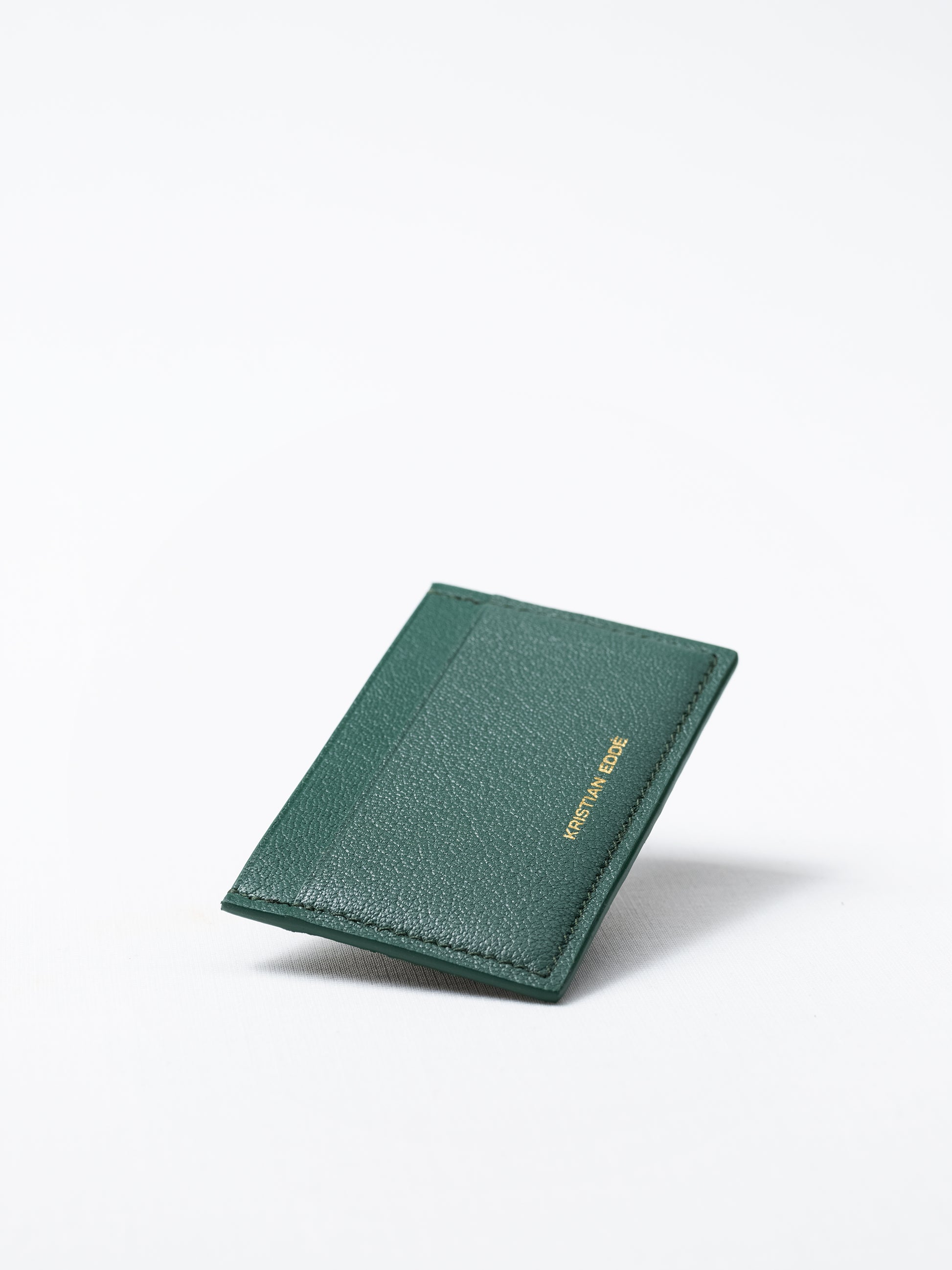 Bothnia green card holder made of salmon leather, back view of gold logo on white background